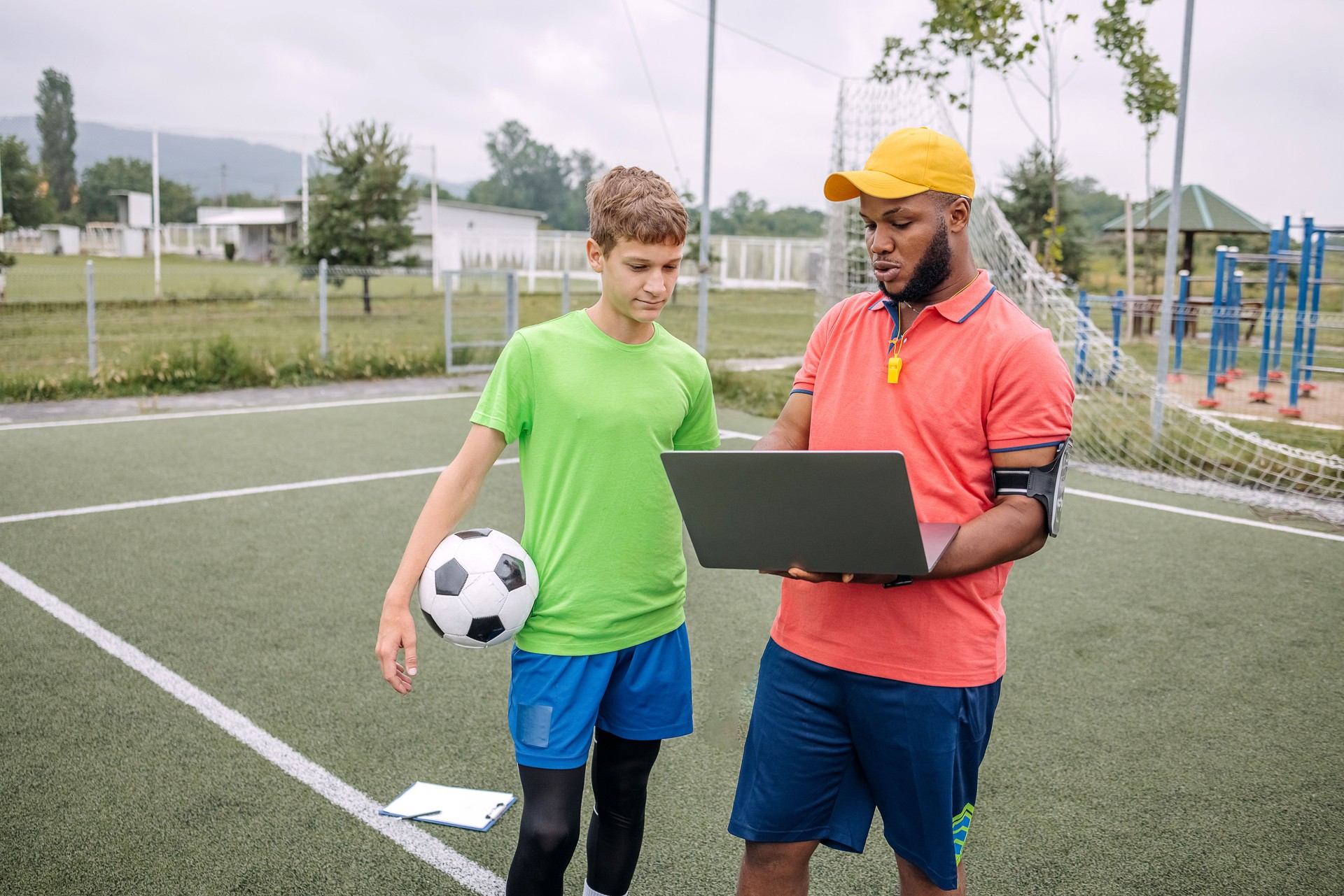 Boy having individual soccer training by the black coach using laptop